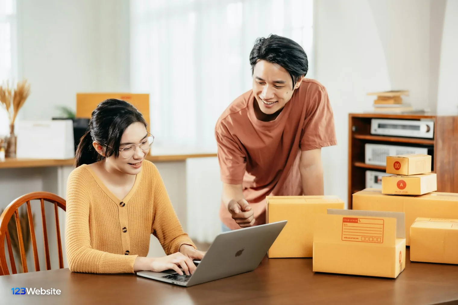 Two shop owners checking orders on a laptop beside Shopify parcels